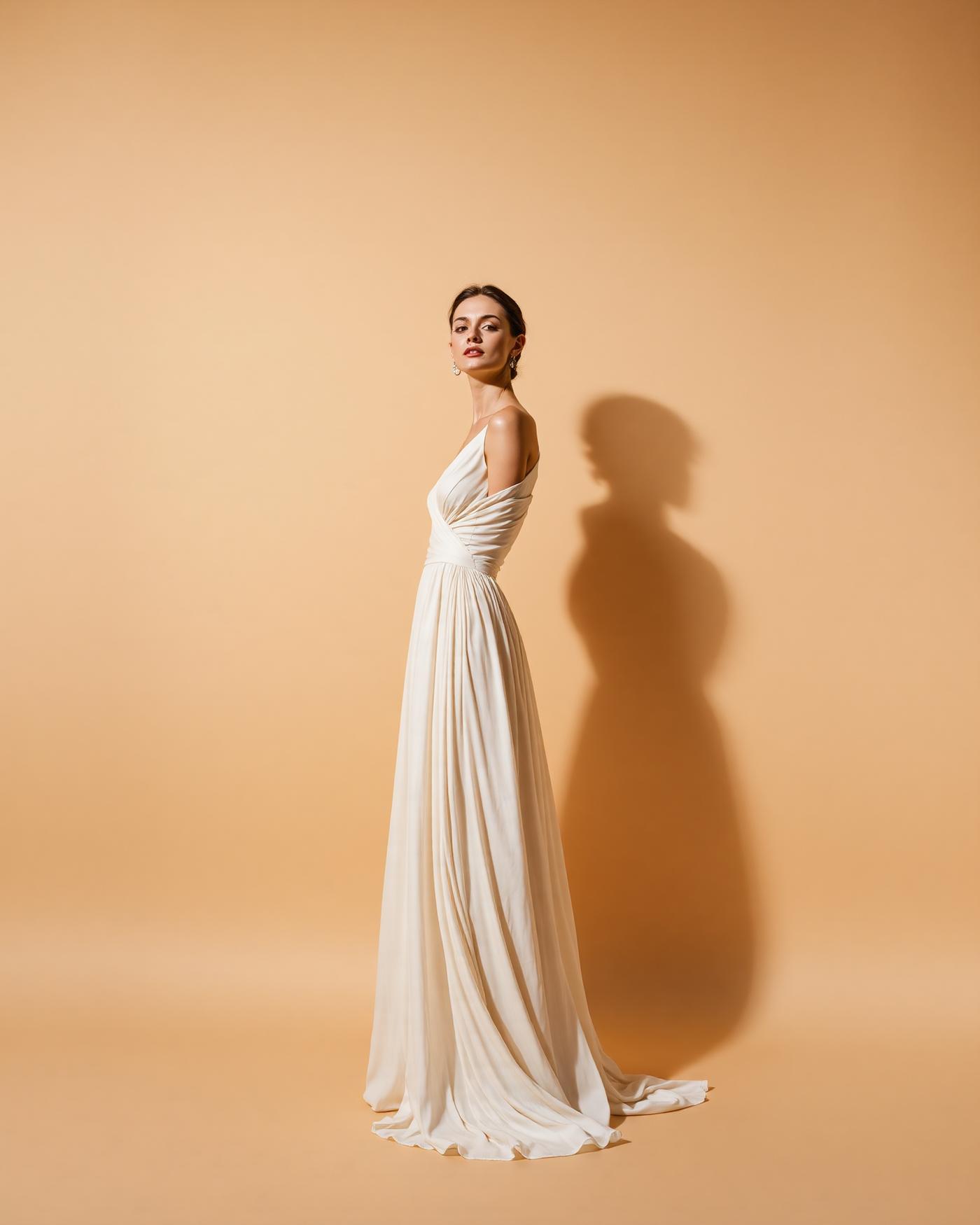 Editorial fashion portrait in a flowing ivory gown against a warm neutral studio backdrop